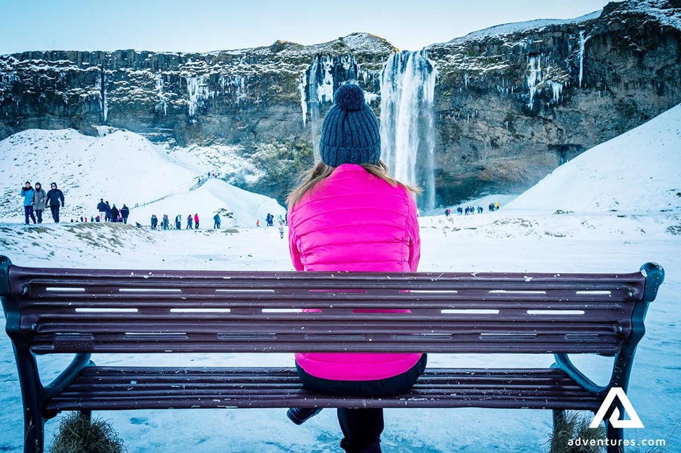 woman on a bench near seljalandsfoss waterfall in winter