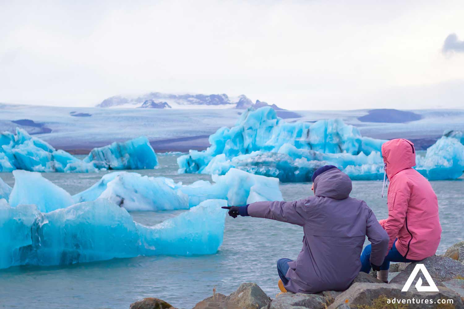 two friends pointing to icebergs in a lagoon in Jokulsarlon