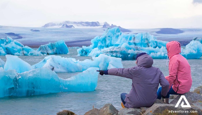 two friends pointing to icebergs in a lagoon in Jokulsarlon