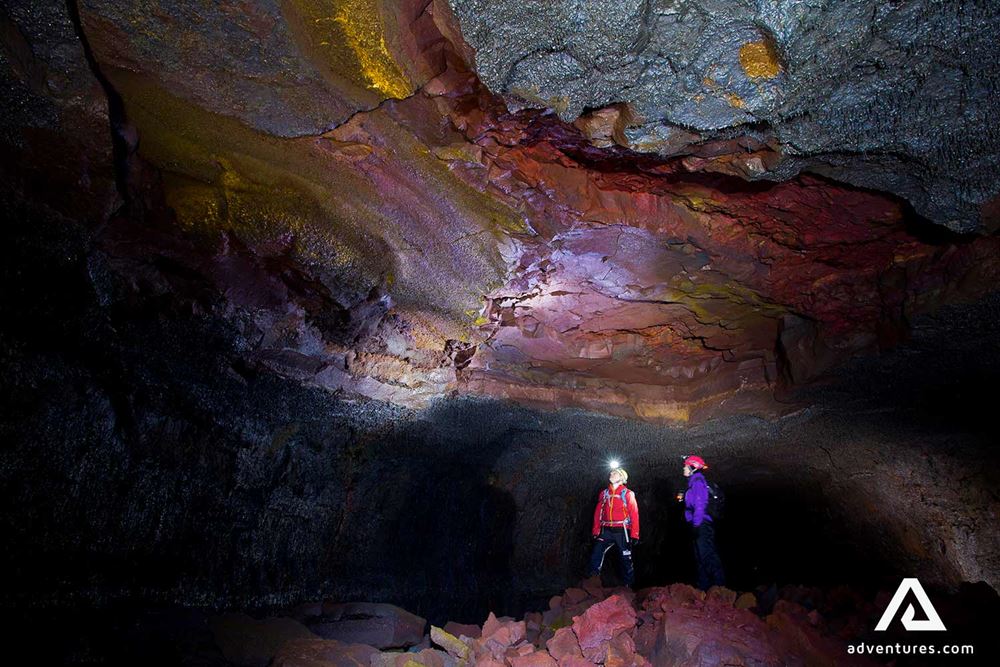 two women inspecting a dark red lava cave