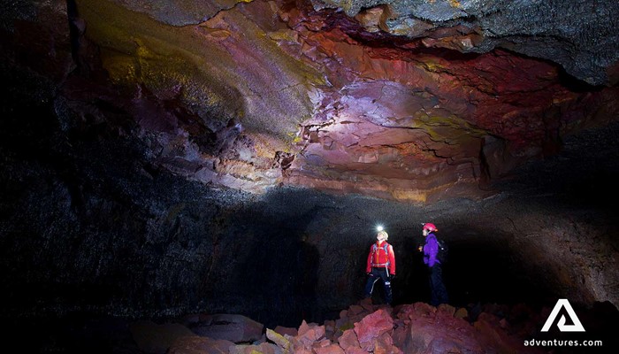 two women inspecting a dark red lava cave vidgelmir