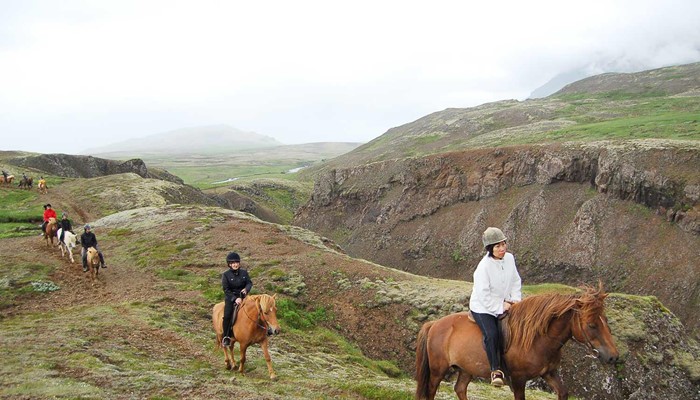 riding horses near a small canyon and a hill