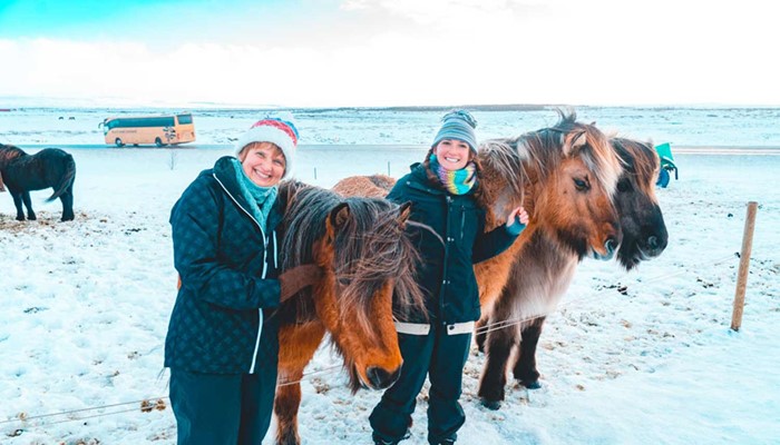 two happy women petting horses and posing for a picture