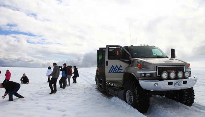 group walking around in snow near a super jeep in iceland