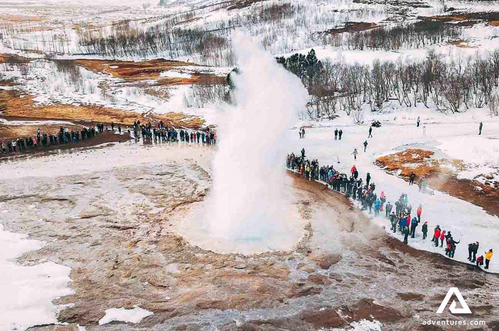 a large group of people watching Geysir eruption in winter