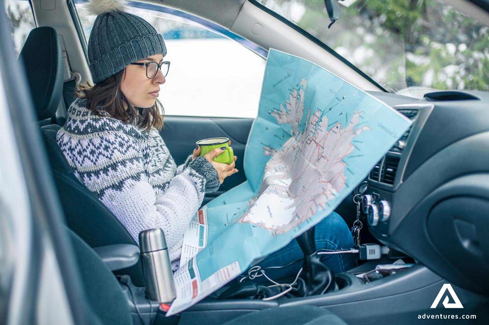 a woman drinking coffee and looking at a map in iceland