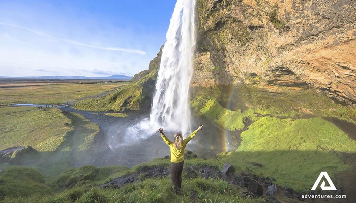 woman standing behind seljalandsfoss waterfall in the south coast