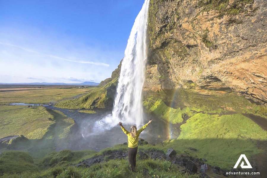 woman standing behind seljalandsfoss waterfall 