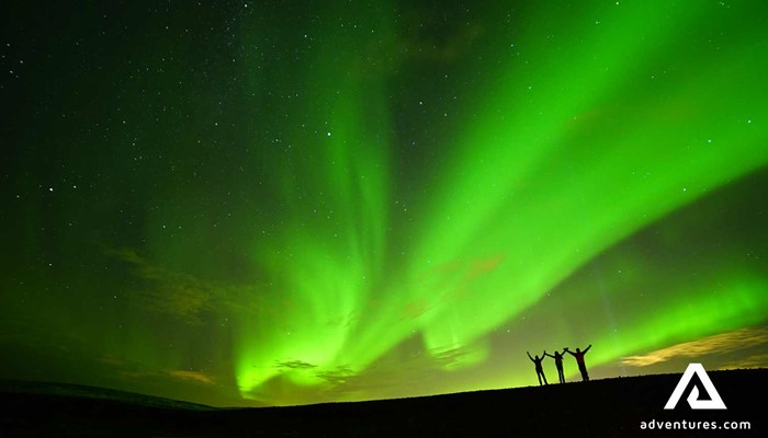 three happy people spreading arms near Northern lights