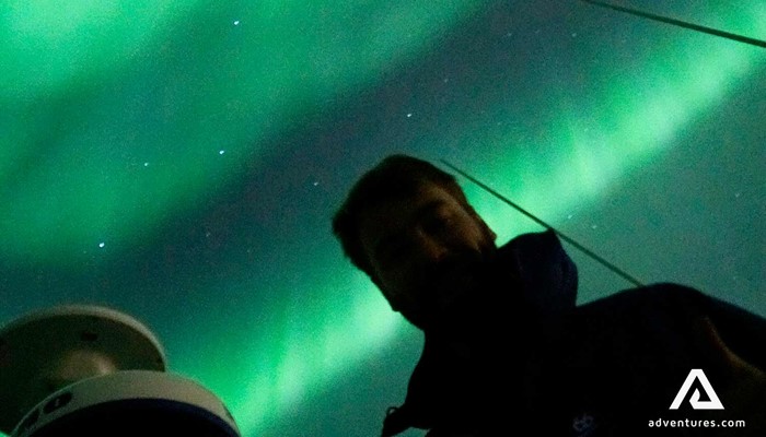 a man near a camera and northern lights in the back