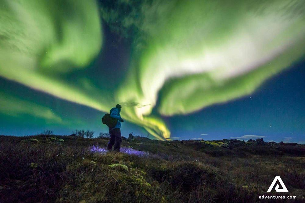 a man hiking on a hill and watching aurora