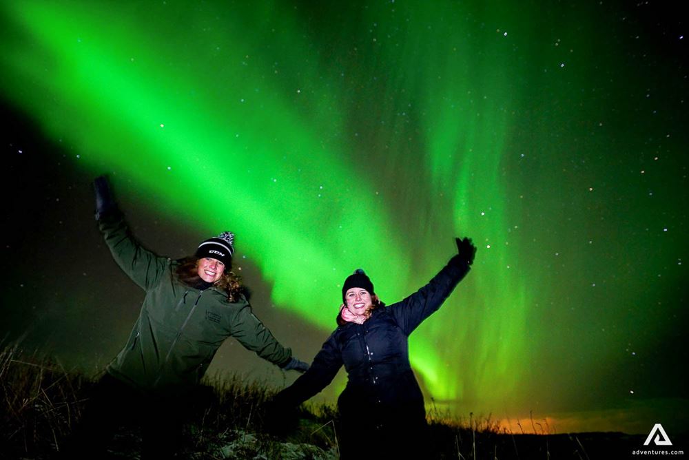 two happy women below aurora borealis
