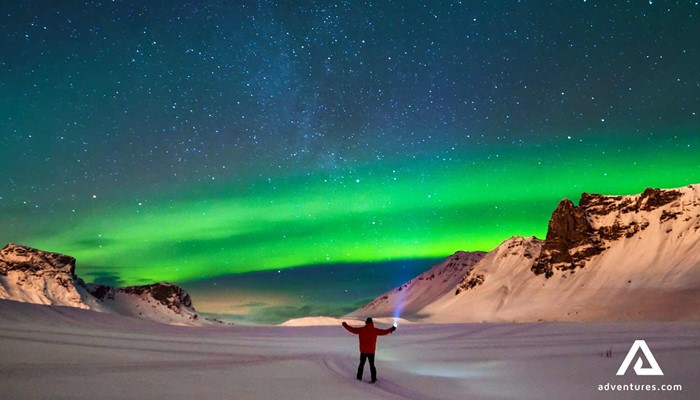 man with a flashlight watching aurora borealis in iceland