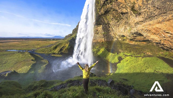 happy woman spreading arms near seljalandsfoss waterfall