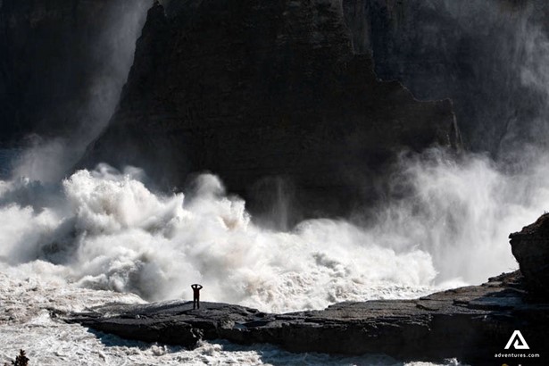 raging stream of water near a person on a shore