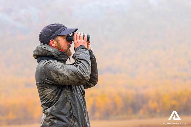 man wildlife watching with binoculars in sweden