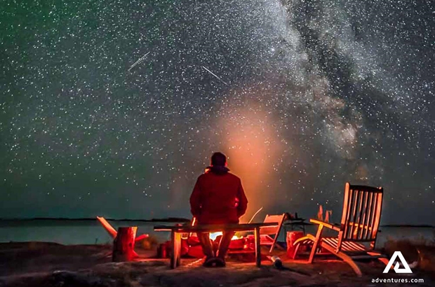 man sitting and watching starry sky with northern lights