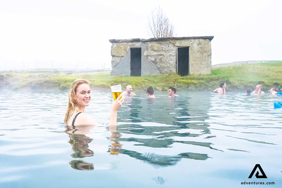 happy woman having a drink in secret lagoon in iceland