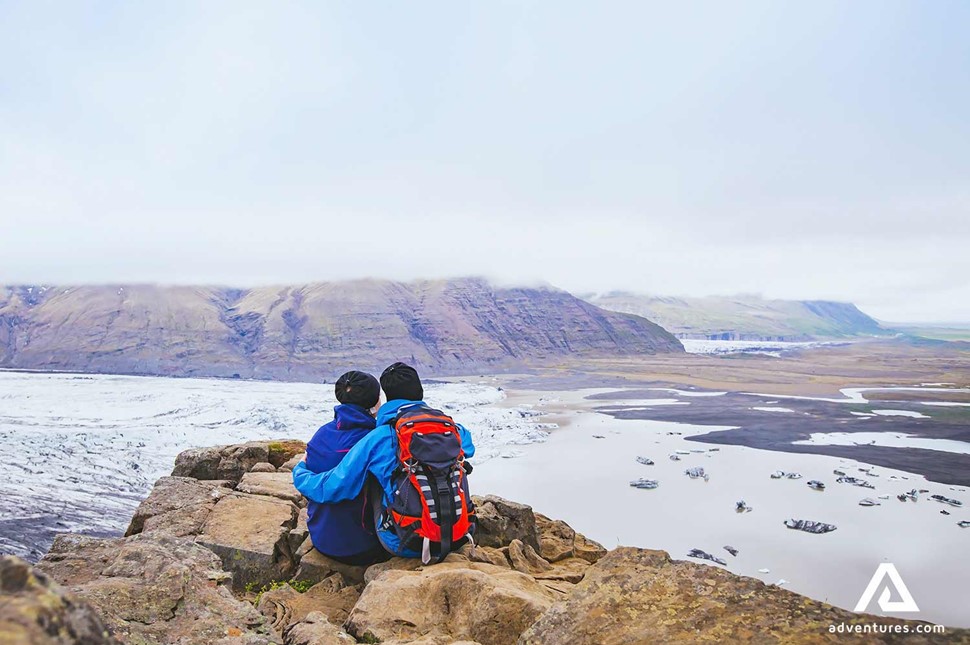 couple sitting near rock cliffs in skaftafell national park