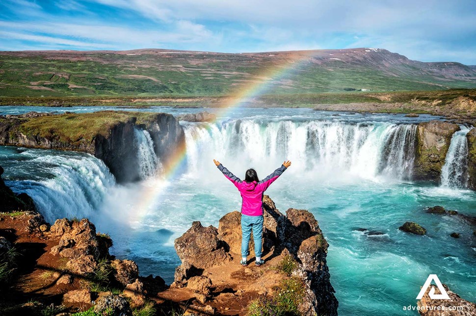 happy woman spreading arms close to godafoss waterfall in iceland