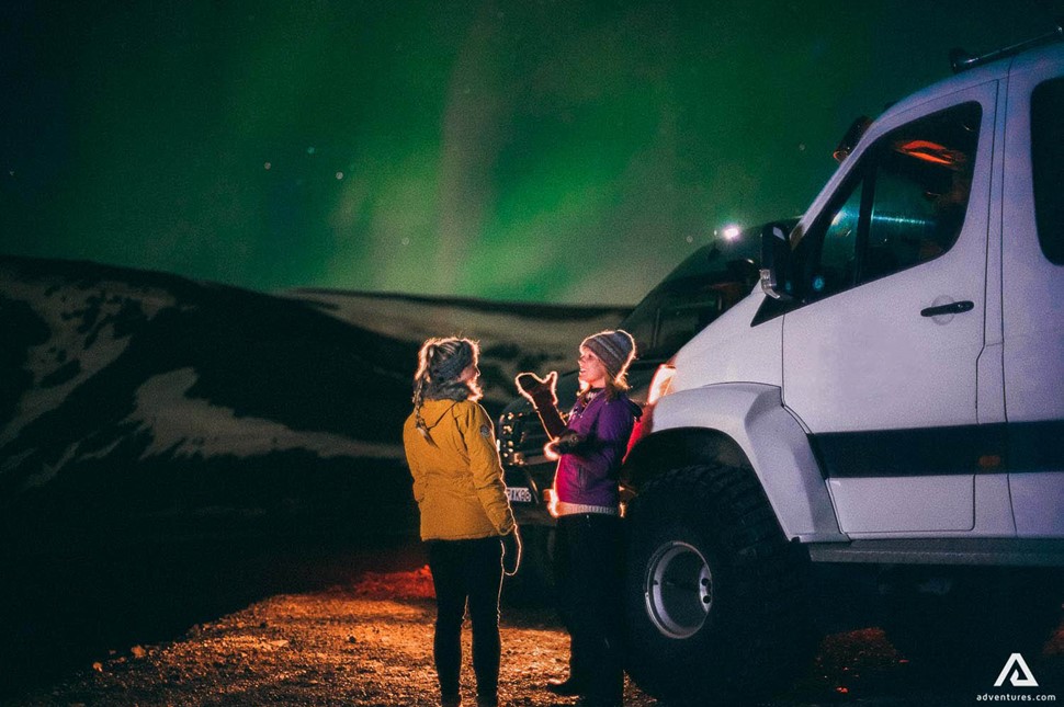 woman talking near a super jeep and northern lights in iceland