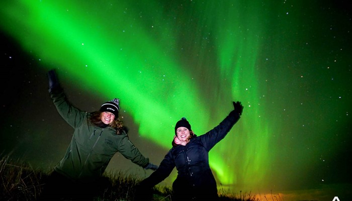 two happy women near northern lights in iceland