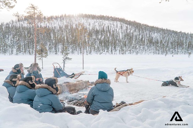 group relaxing after dog sledding near a campfire