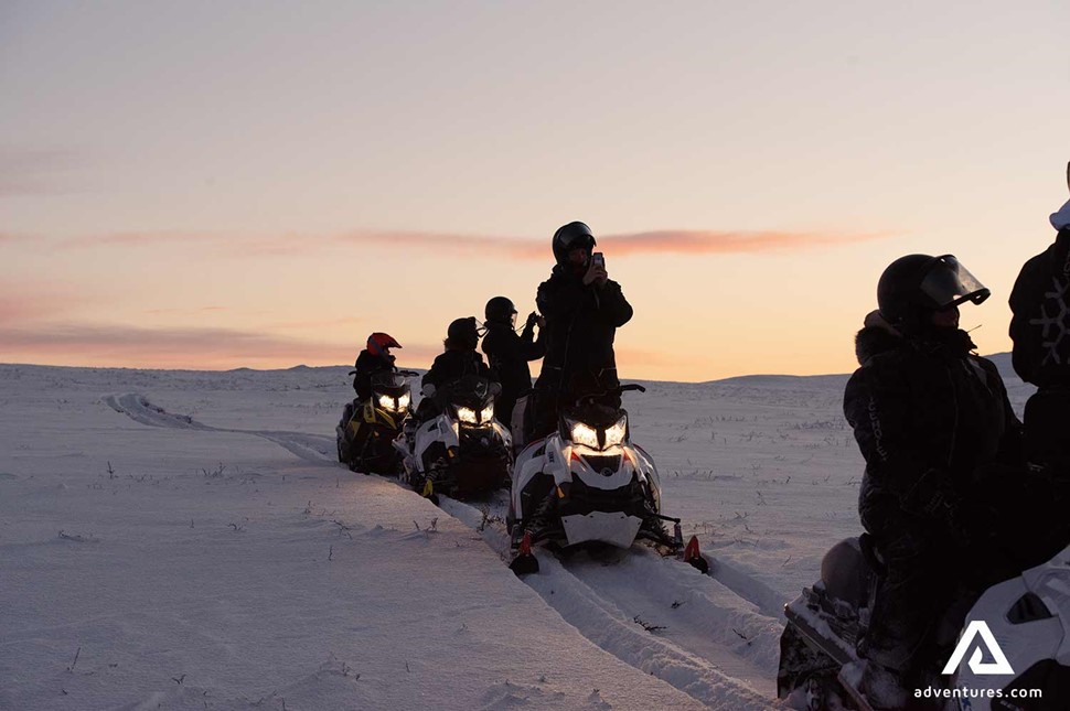 small group enjoying sunset on snowmobiles in sweden