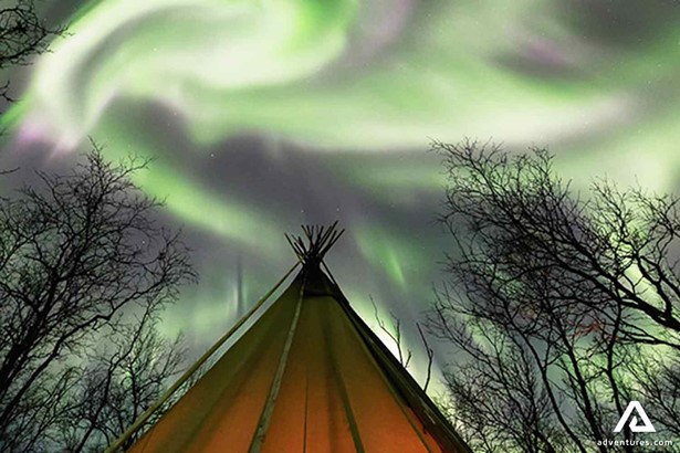 bright green and purple northern lights above a teepee