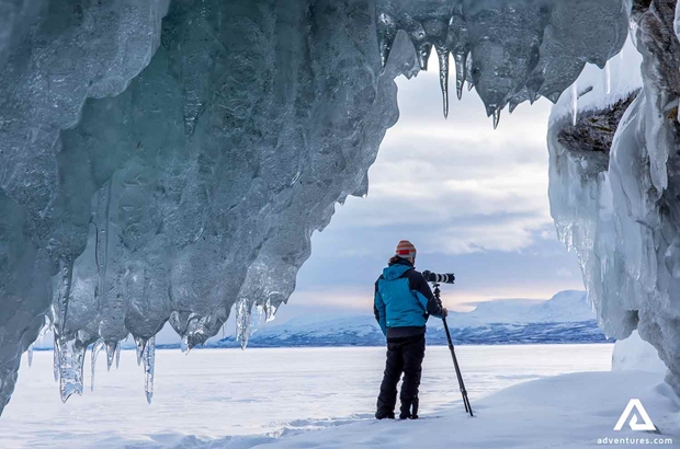 photographer near a frozen waterfall in lapland in winter