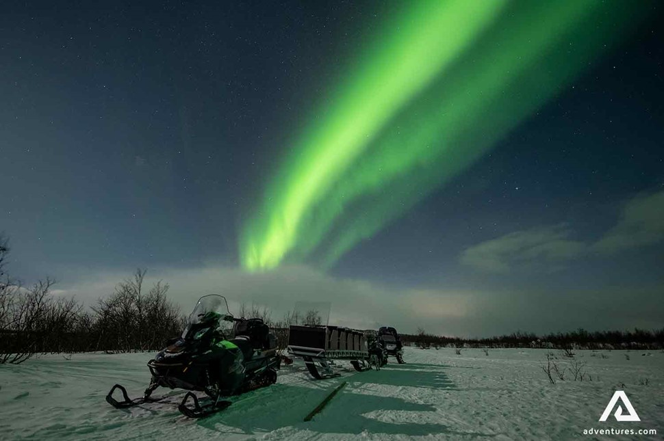 snowmobiles lined up in winter with northern lights above in sweden