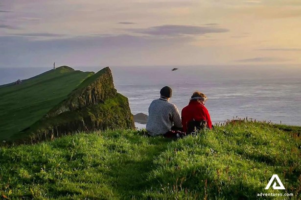 two friends sitting and watching sunset in faroe islands