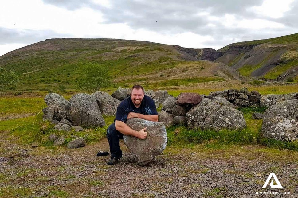 man trying to pick up a large rock near husafell