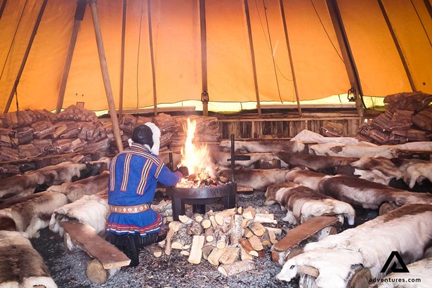 sami man lighting a fire in a large tent