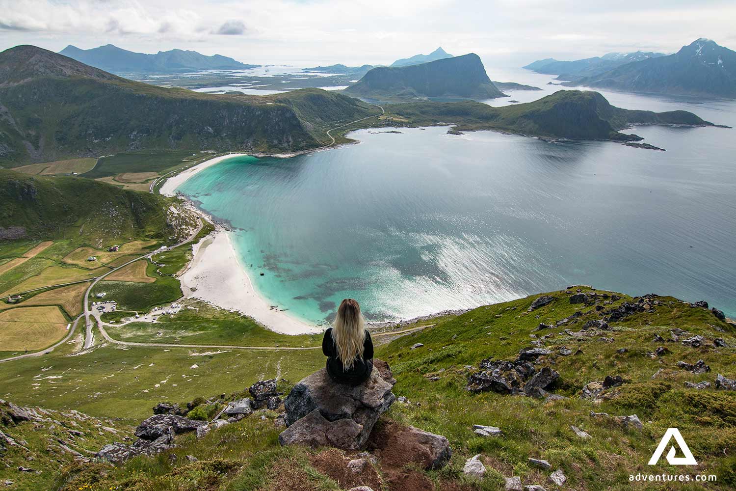 woman sitting on a mountain top near haukland beach in norway at summer