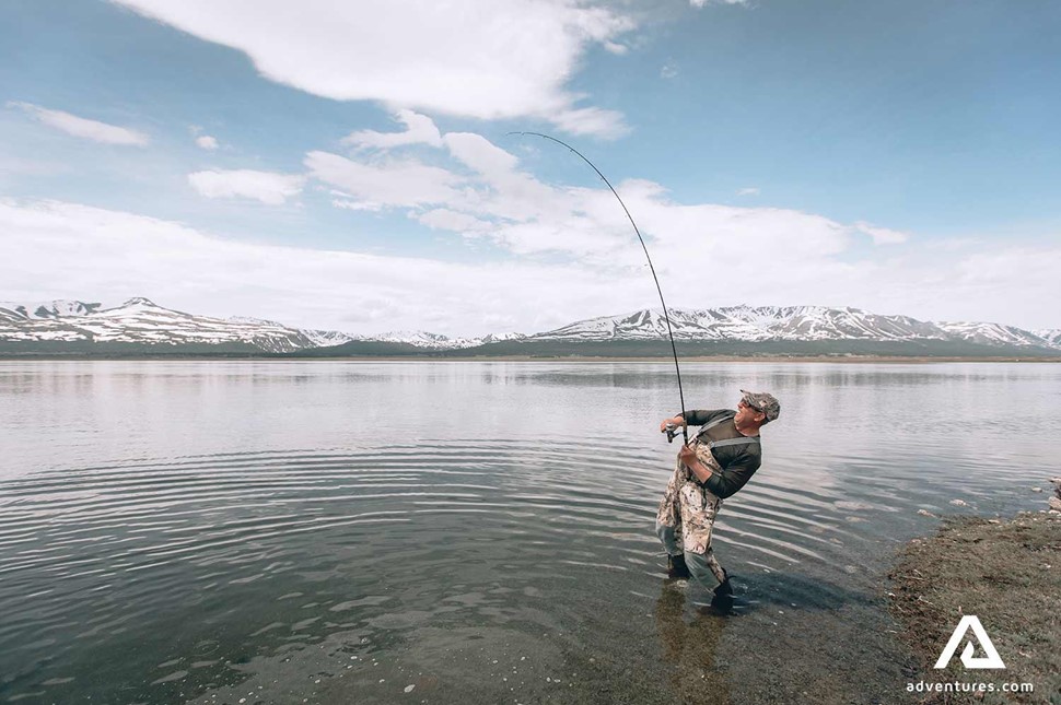 man fly fishing in a lake with snowy mountains in the background