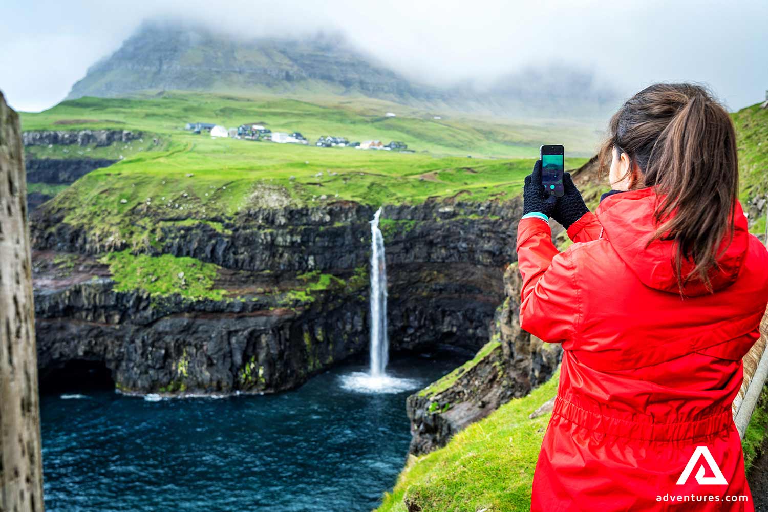 woman taking pictures of the mulafossur waterfall in faroe islands