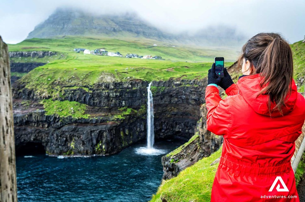 woman taking pictures of the mulafossur waterfall in faroe islands