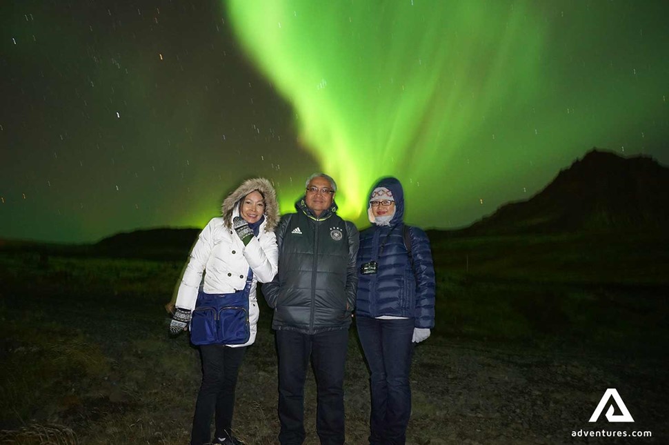 happy friends watching northern lights in iceland at winter