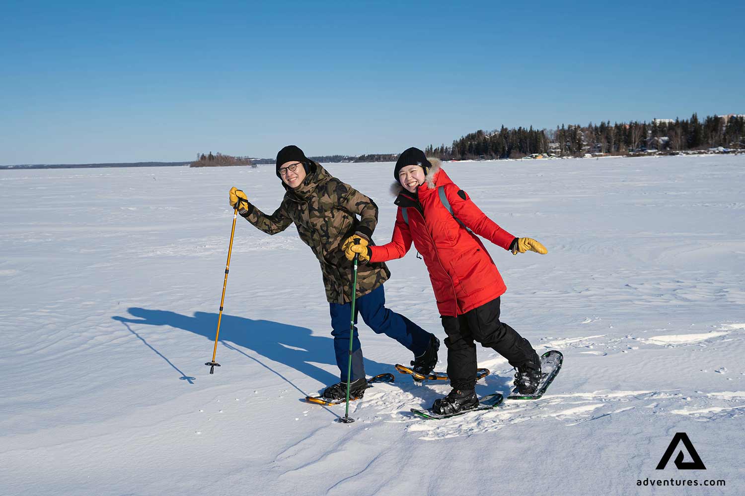 happy friends enjoying snowshoeing at frozen lake