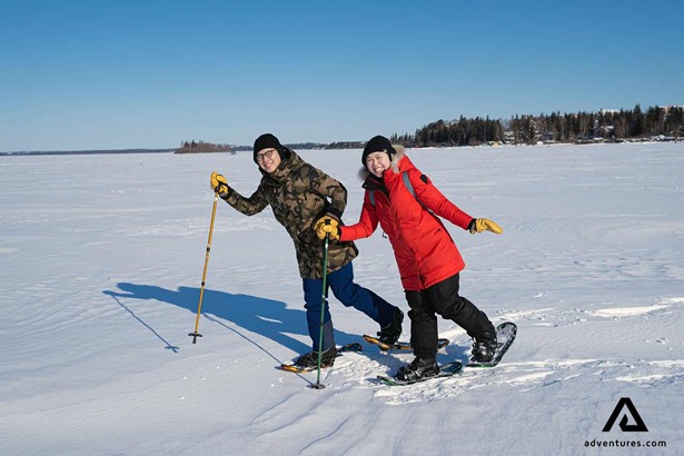 happy friends enjoying snowshoeing at frozen lake