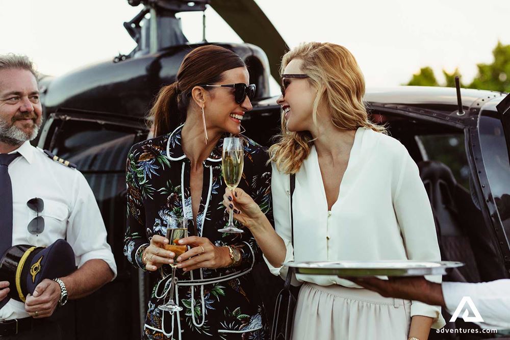 happy friends drinks champagne before helicopter flight