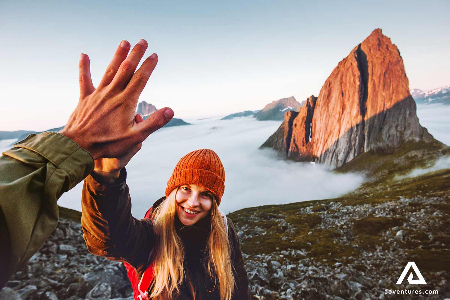 highfiving a woman after summiting a mountain above clouds