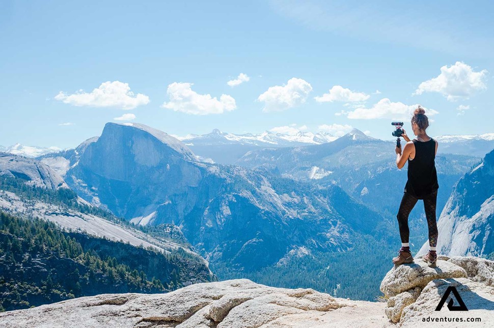 a woman taking video with her camera on a mountain top after hiking