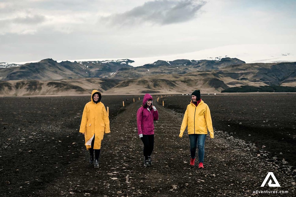 women in yellow jackets walking at black beach