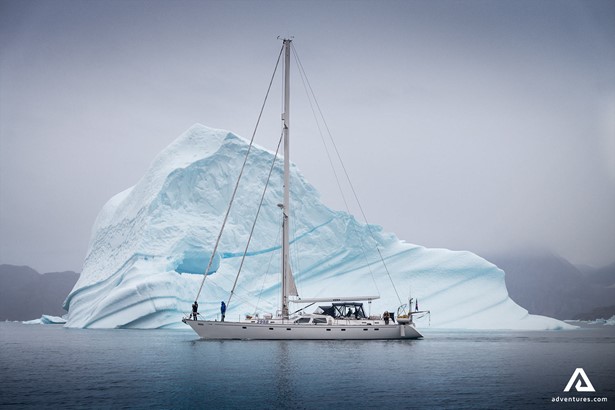 Sailing Boat Swims by Giant Iceberg