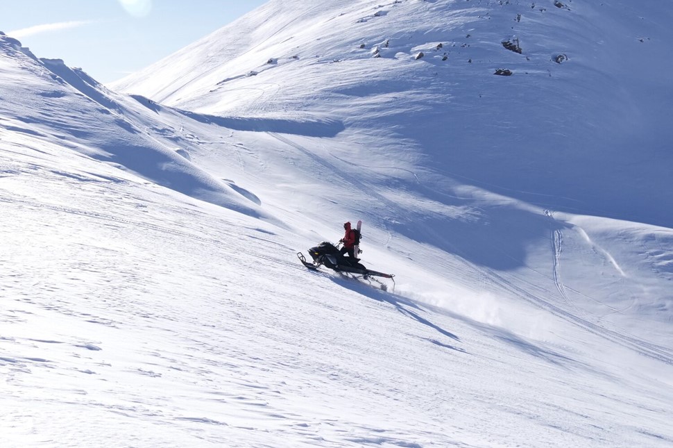 Person driving a snowmobile up the snowy slope