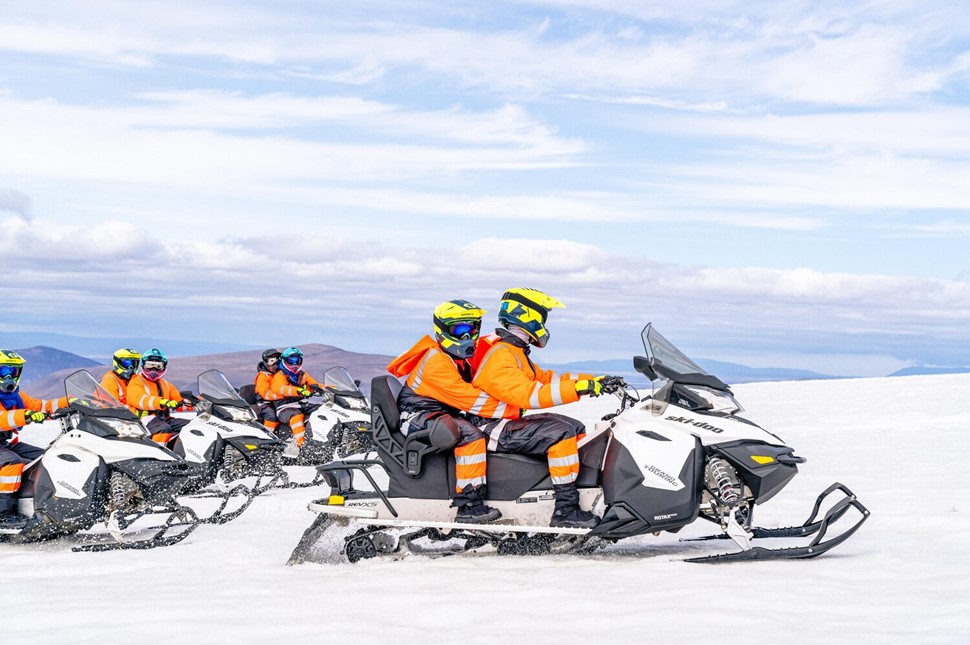 People snowmobiling on glacier in pairs