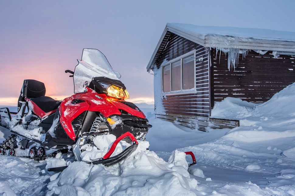 Snowmobile rests beside a frosty cabin as dusk paints the sky