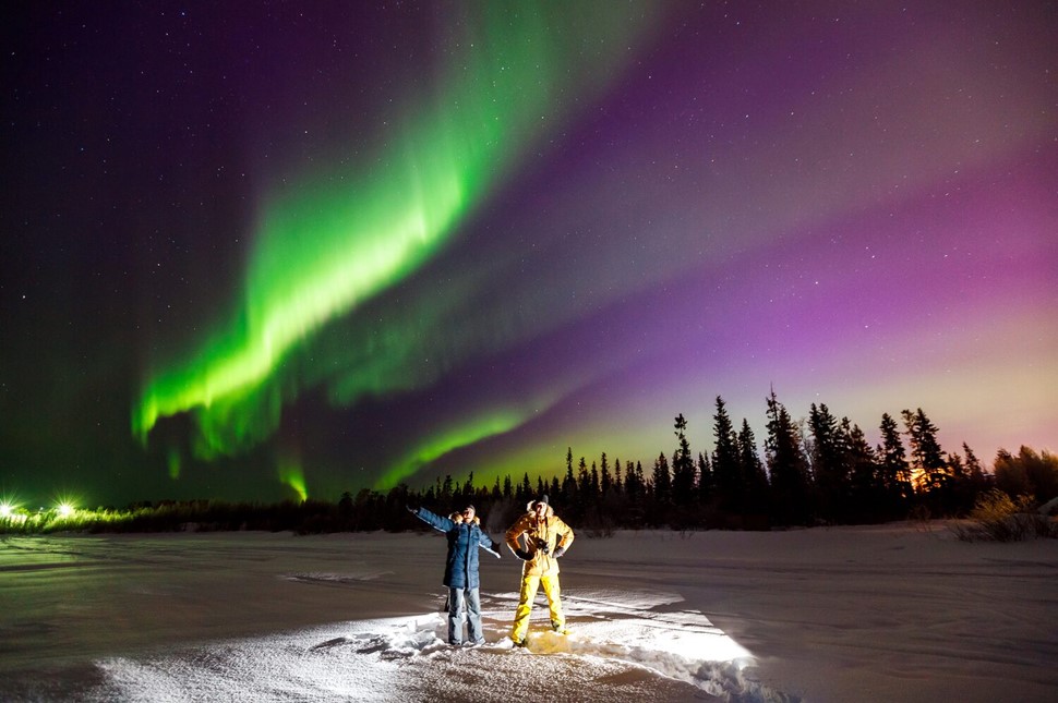 Two young men are posing against shining northern lights sky